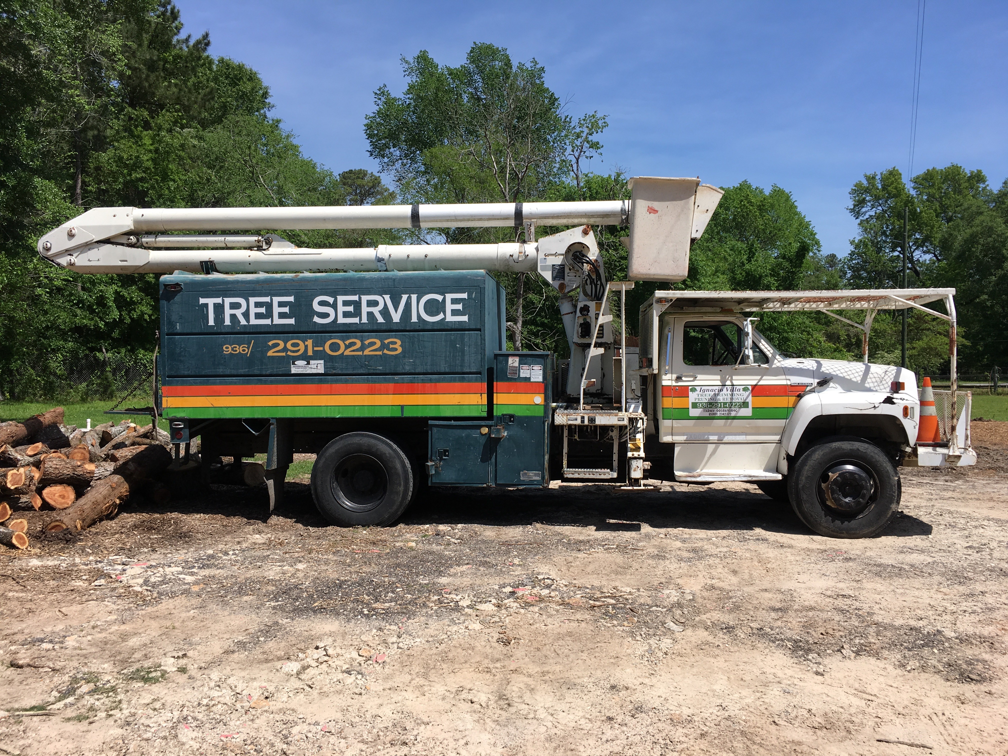 Ignacio Villa's Tree Service bucket truck with raised boom next to freshly cut logs in Huntsville, TX