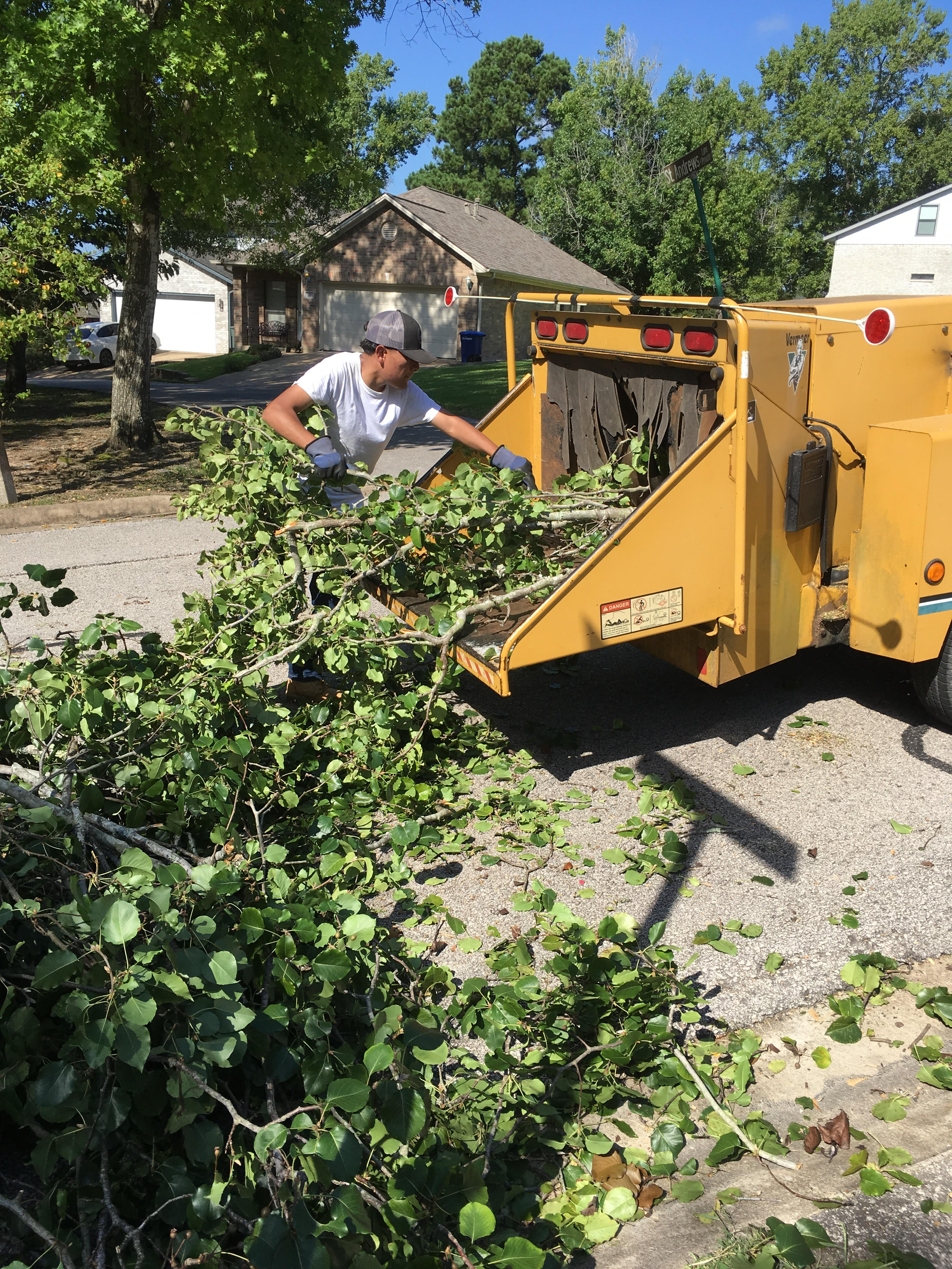 Crew loading tree branches into a wood chipper truck during debris clean-up in Huntsville, TX